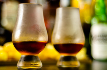 glass of whiskey with ice cubes and salty snacks on the background of the bar