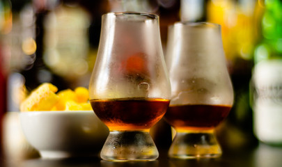 glass of whiskey with ice cubes and salty snacks on the background of the bar