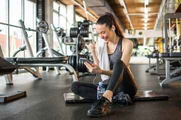 Cheerful young woman reading good news on mobile phone and celebrating success during workout break...