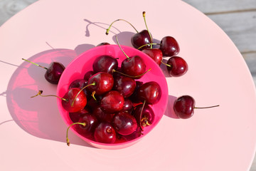 Ripe cherry in a bright pink bowl on a pink table. Several cherries lie on the table. Picking berries. Summer harvest.