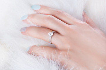Diamond engagement wedding ring on female finger and hand on fur white background. Jewelry and...
