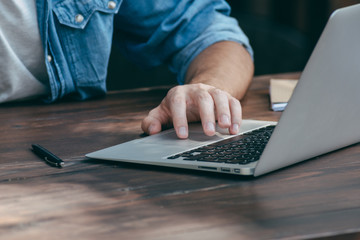 Men's hands are printed on a laptop on a wooden brown table in a cafe with free Wi-Fi, in the foreground a notebook. The concept for a freelancer works anytime, anywhere. Side view, concept.