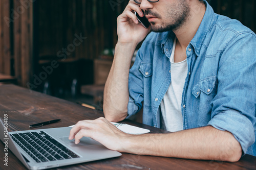 A Man In A White T Shirt And Blue Shirt Is Talking On The Phone