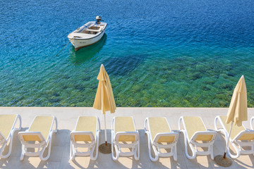 Boat in the turquoise Adriatic sea with the chairs and umbrellas on the pier