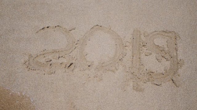 New year 2019 handwritten is appearing after wahing away 2018 y on sandy beach.
