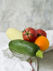 Glass plate with vegetables - zucchini, cucumber, red and orange tomatoes, on a gray background. Copy space, close up