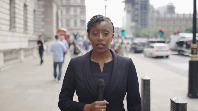 Female news reporter talking into camera holding a microphone in the city