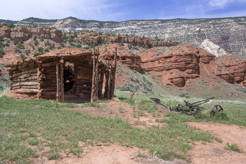 Sheep herders pioneer log cabin with mud and grass roof and antique sickle mower to cut meadow grass in red stone canyon of Colorado, USA