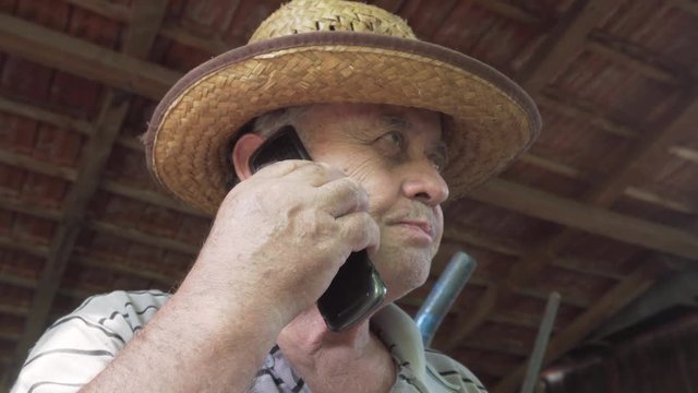 Old Man Wearing A Straw Hat Talking Over A Flip Phone And Hanging Up