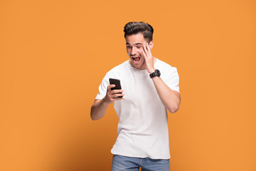 Smiling handsome man with mobile phone on yellow background.