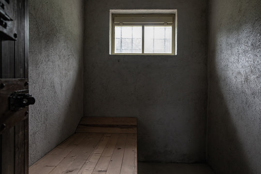 Small prison concrete cell with one small window and one wooden pallet.