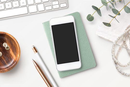 Bright feminine smartphone mockup with mint notebook, eucalyptus twigs, accessories and a wooden bowl on a white boho styled desk. Flat lay. - Powered by Adobe