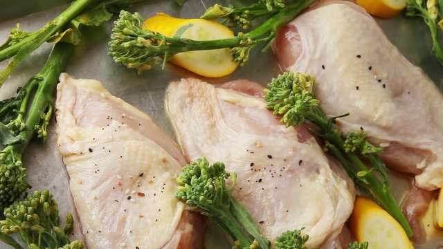 A woman sprinkles seasonings over raw chicken breasts and vegetables on a sheet pan