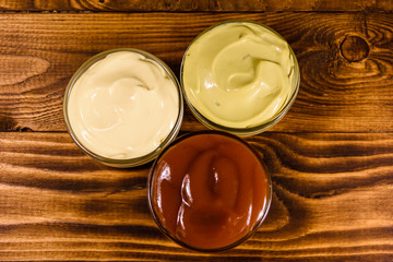Different sauces in glass bowls on wooden table. Top view