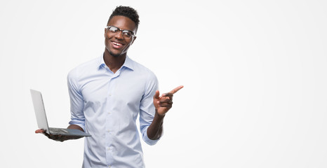 Young african american businessman using computer laptop very happy pointing with hand and finger to the side