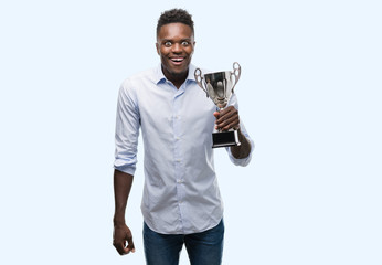 Young african american man holding trophy scared in shock with a surprise face, afraid and excited with fear expression