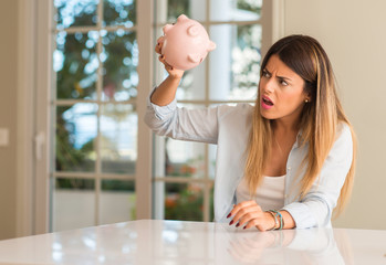 Beautiful young woman wondering how much money has into piggy bank at home, broke. Business concept.