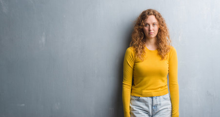 Naklejka premium Young redhead woman over grey grunge wall with a confident expression on smart face thinking serious