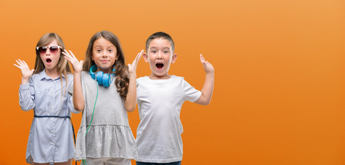 Group of boy and girls kids over orange background very happy and excited, winner expression celebrating victory screaming with big smile and raised hands