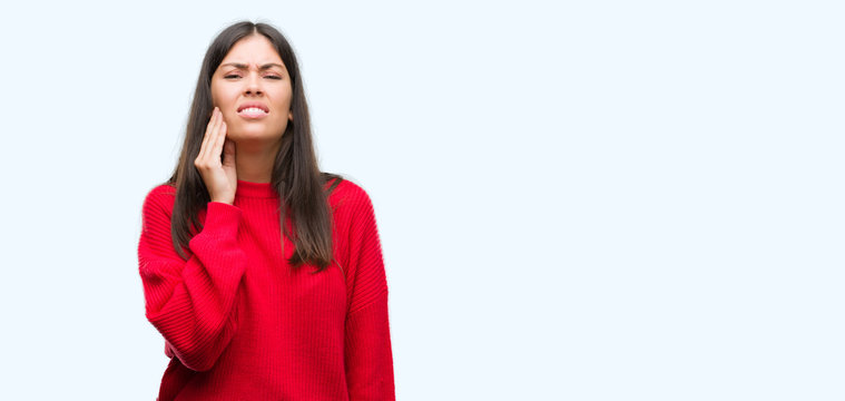 Young beautiful hispanic wearing red sweater touching mouth with hand with painful expression because of toothache or dental illness on teeth. Dentist concept.