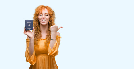 Young redhead woman holding passport of Germany pointing and showing with thumb up to the side with happy face smiling