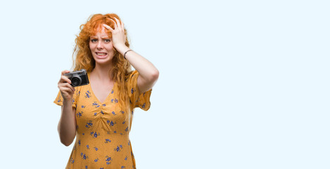 Young redhead woman taking pictures holding vintage camera stressed with hand on head, shocked with shame and surprise face, angry and frustrated. Fear and upset for mistake.