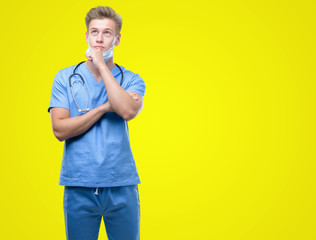 Young handsome blond doctor serious face thinking about question, very confused idea