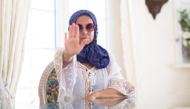Middle age brunette arabian woman wearing colorful hijab at luxury house with open hand doing stop sign with serious and confident expression, defense gesture