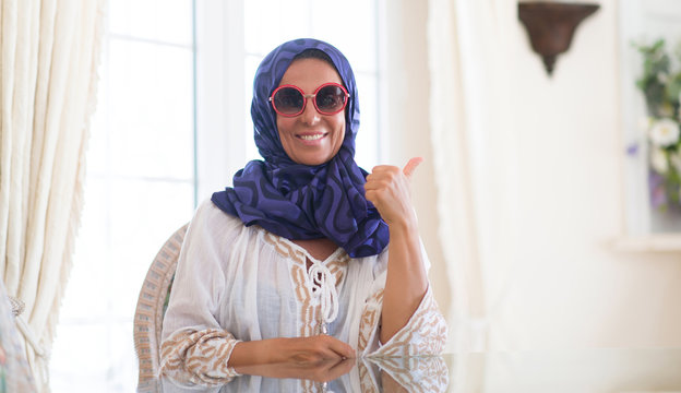 Middle age brunette arabian woman wearing colorful hijab at luxury house happy with big smile doing ok sign, thumb up with fingers, excellent sign