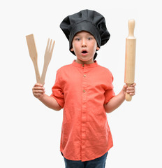 Fototapeta premium Dark haired little child wearing chef uniform scared in shock with a surprise face, afraid and excited with fear expression