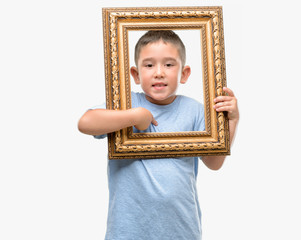Dark haired little child holding frame with surprise face pointing finger to himself