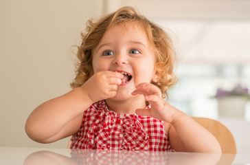 Beautiful blonde child with blue eyes smiling and eating candy at home. © Krakenimages.com