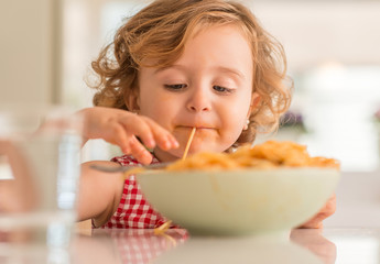 Beautiful blond child eating spaghetti with hands at home