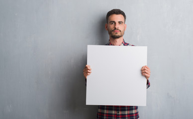 Young adult man over brick wall holding banner with a confident expression on smart face thinking...