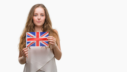 Young blonde woman holding flag of UK with a confident expression on smart face thinking serious