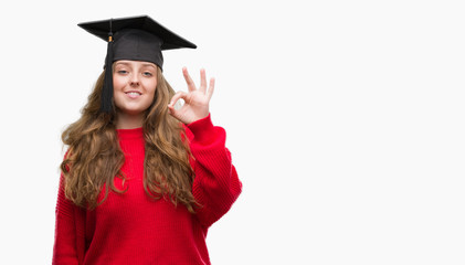 Young blonde woman wearing graduation cap doing ok sign with fingers, excellent symbol