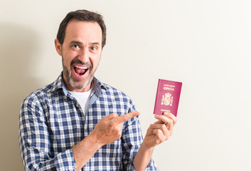 Senior man holding spanish passport very happy pointing with hand and finger