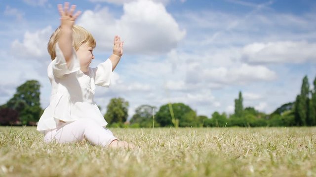 Happy toddler clapping and waving hands in a park  outside in the sun, in slow motion