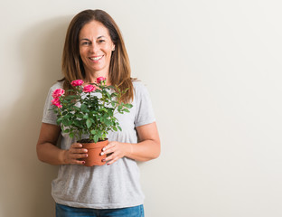 Middle age woman holding roses flowers on pot with a happy face standing and smiling with a confident smile showing teeth