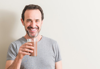 Senior man drinking chocolate milk shake with a happy face standing and smiling with a confident...