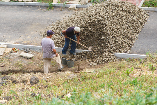 Two workers are engaged in construction. Working with a shovel about a pile of stones.