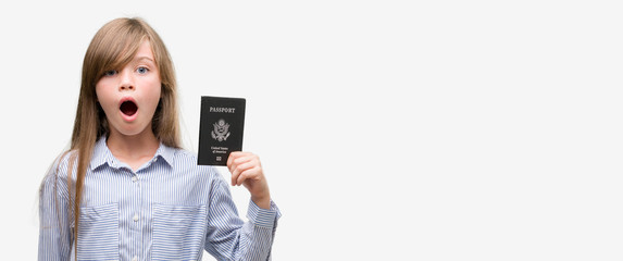 Young blonde toddler holding american passport scared in shock with a surprise face, afraid and excited with fear expression