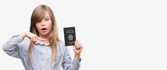 Young blonde toddler holding italian passport very happy pointing with hand and finger