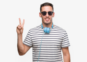 Handsome young man wearing headphones showing and pointing up with fingers number two while smiling confident and happy.