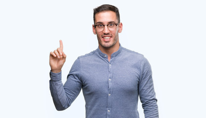 Handsome young elegant man wearing glasses showing and pointing up with finger number one while smiling confident and happy.