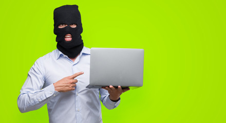 Business hacker man holding a computer laptop very happy pointing with hand and finger