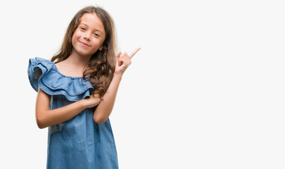 Brunette hispanic girl wearing denim dress very happy pointing with hand and finger to the side