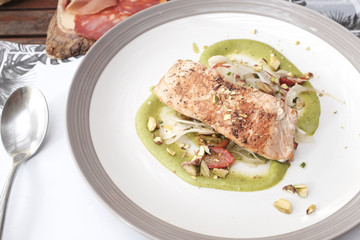 Grilled salmon steak served with green pesto sauce, fresh tomatoes, onion, on top with pistachio