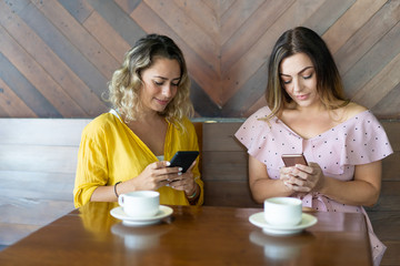 Smiling young woman addicted to social media. Beautiful female friends playing games on smartphones...