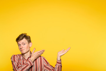 smiling young man pointing sideways with hands as if showing to smth. portrait of a guy on yellow...